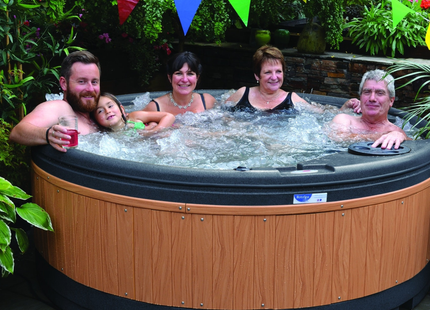 Family and friends enjoying a RotoSpa QuatroSpa round hot tub with teak panels in a garden