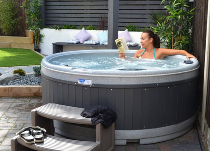 Woman relaxing in a RotoSpa QuatroSpa round hot tub with matching steps on a garden patio