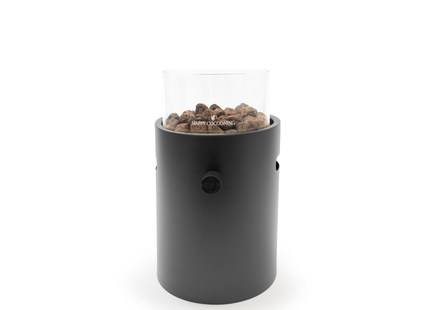 A black cylindrical portable fire pit with a clear glass wind guard and visible wood pellets, set against a plain white background.