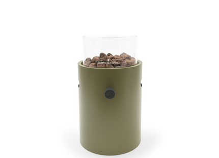 A modern outdoor fire pit with an olive green cylindrical body, clear glass wind guard, with brown decorative stones. The brand name is printed on the front of the glass.